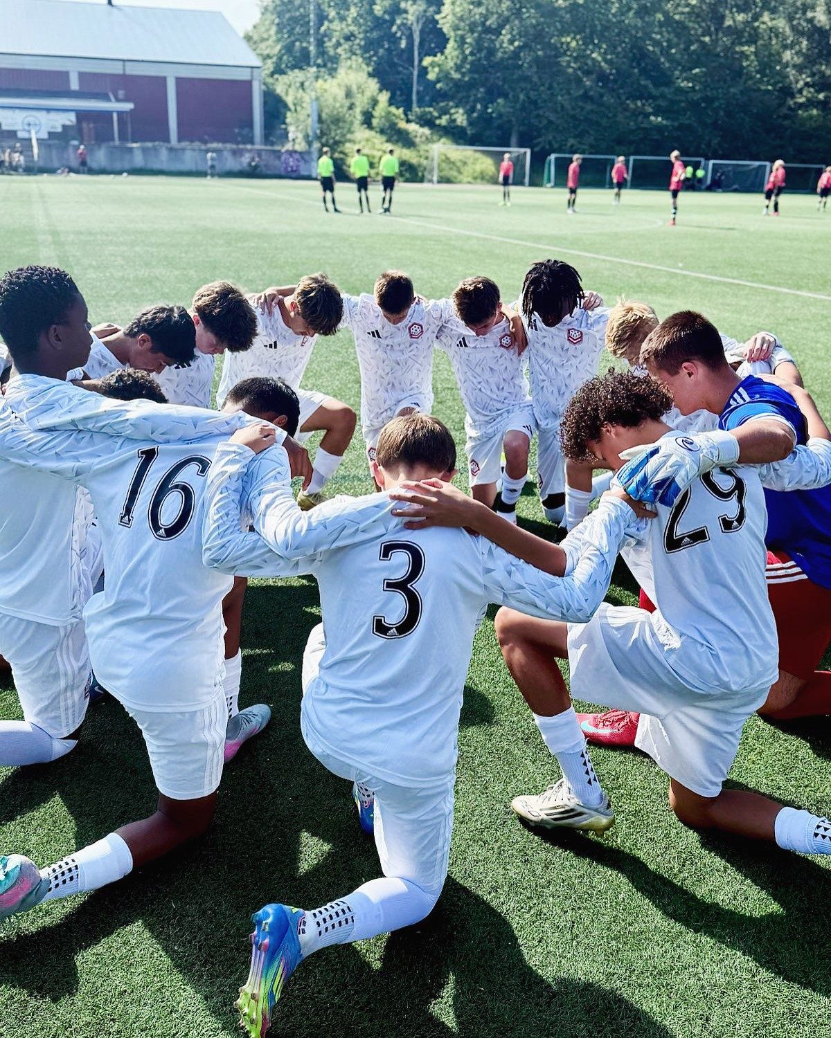The team kneels arm in arm in a huddle before a match
