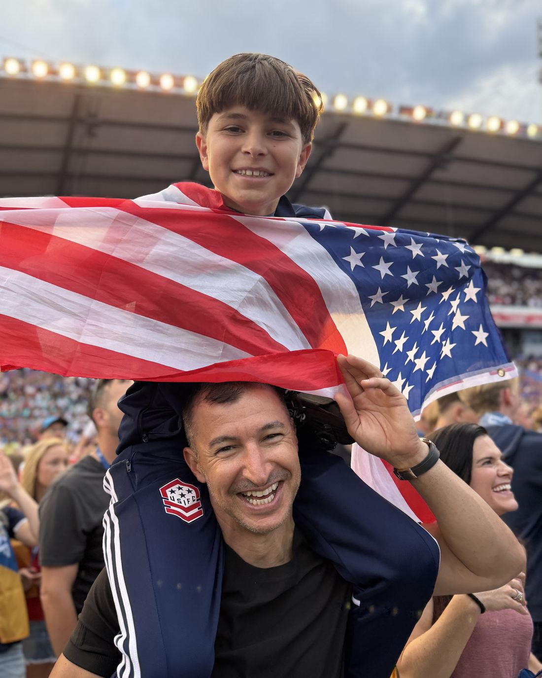 A boy on shoulders holds the American flag in the stadium crowd