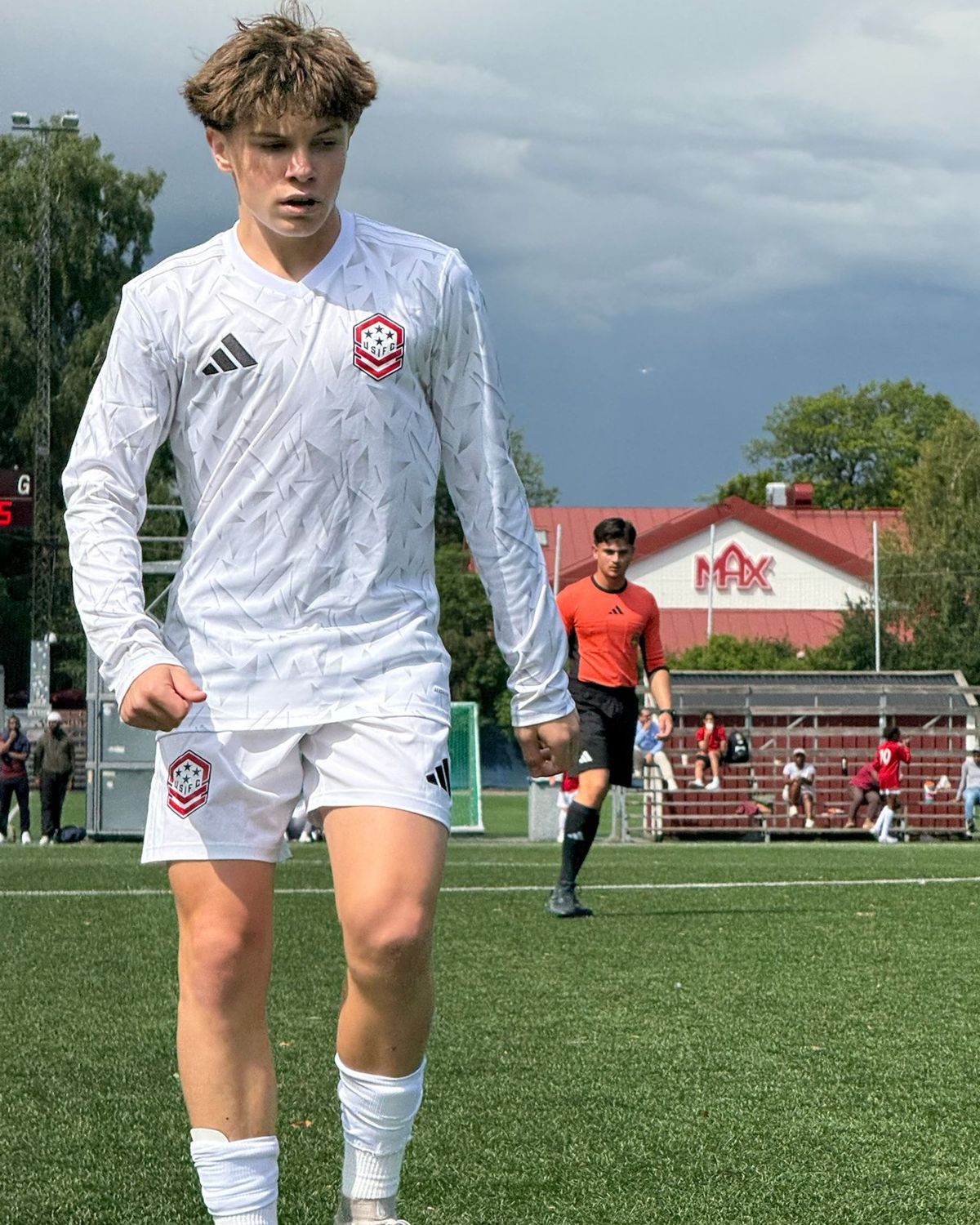 A USIFC player in the white away kit walks off the pitch under a storm sky